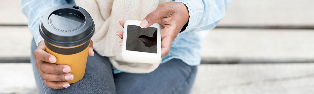 Woman using phone while holding coffee.