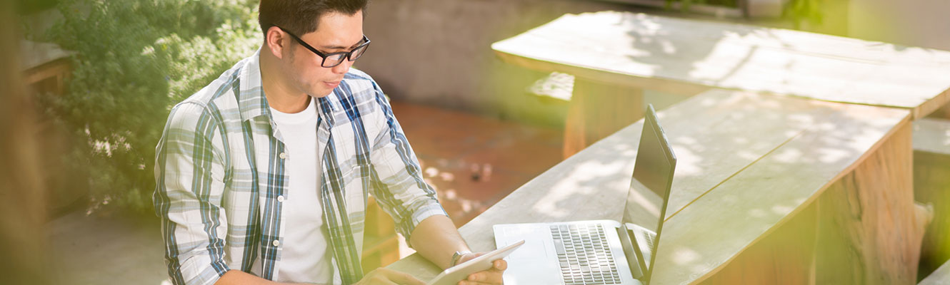 Man using tablet and computer outdoors.